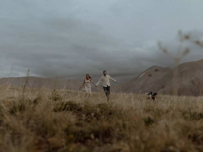 A pair of fiancées runs through a field in Colorado with their dog.