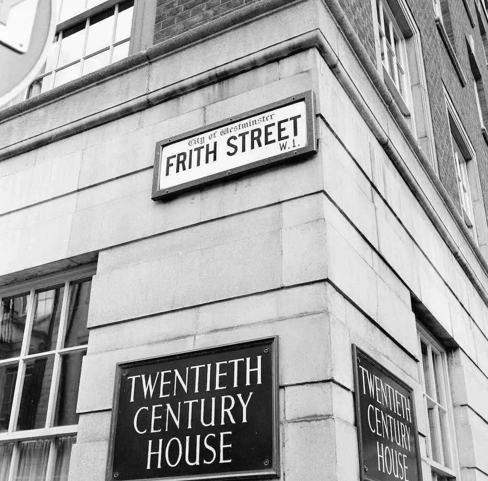 A black-and-white photograph showing the corner of Tewntith Century House in 1956, including its Frith Street street sign.