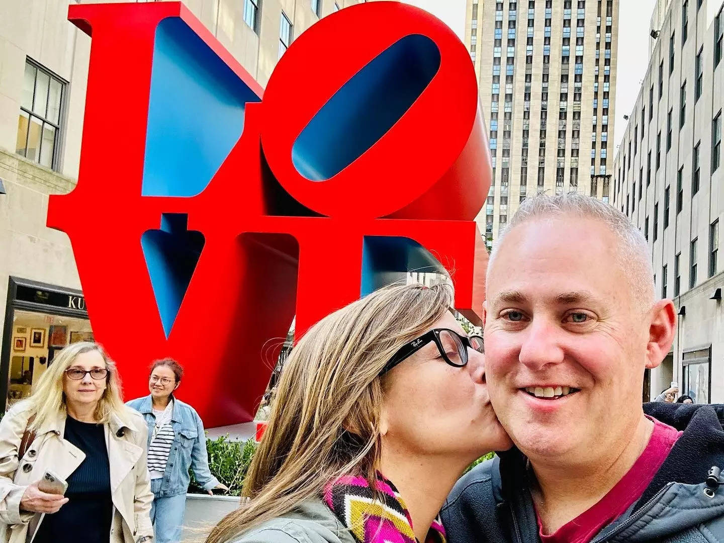 Woman kissing man on the street in New York City in front of the Love statue.