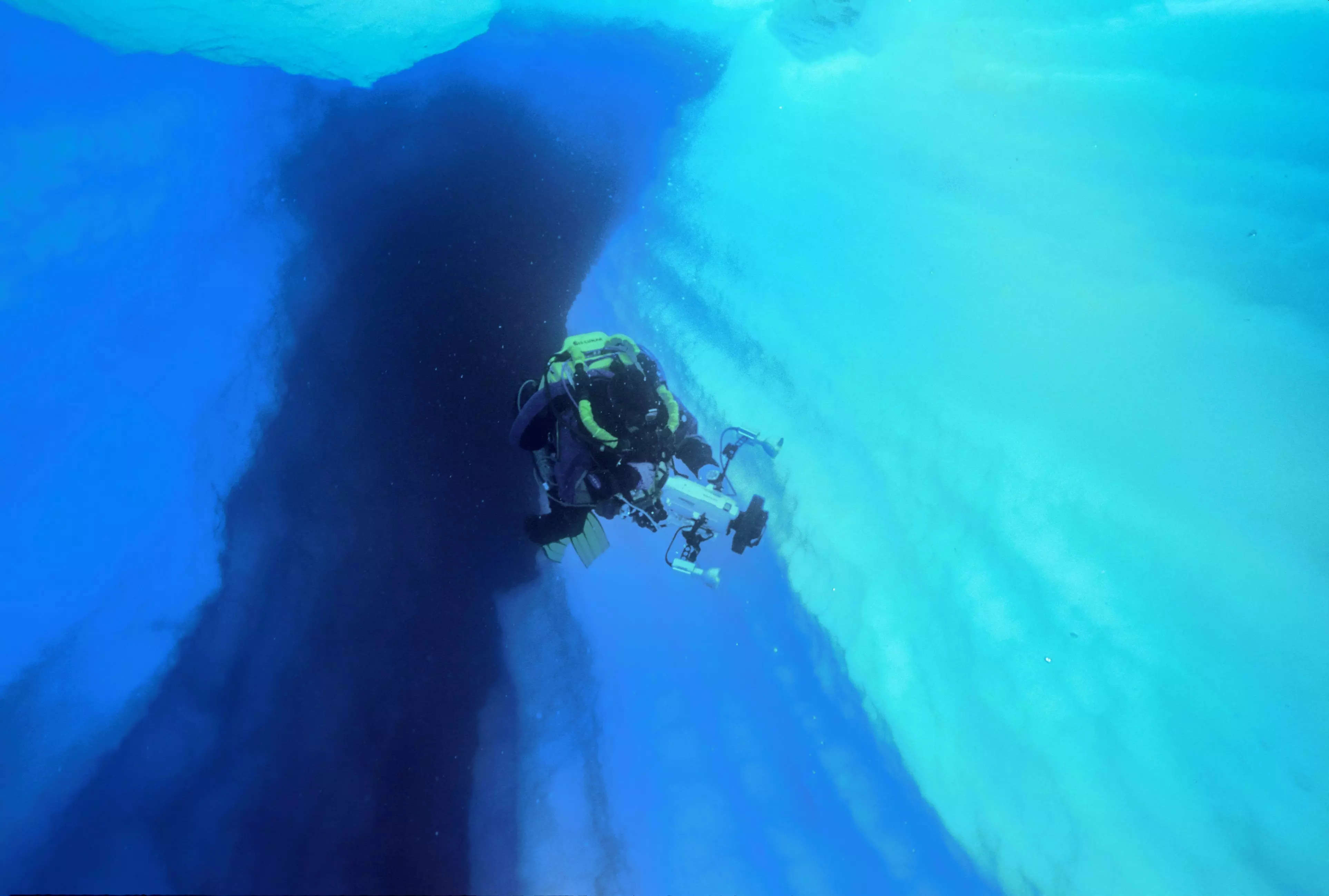 A diver swims with a camera through a crevasse in iceberg B15