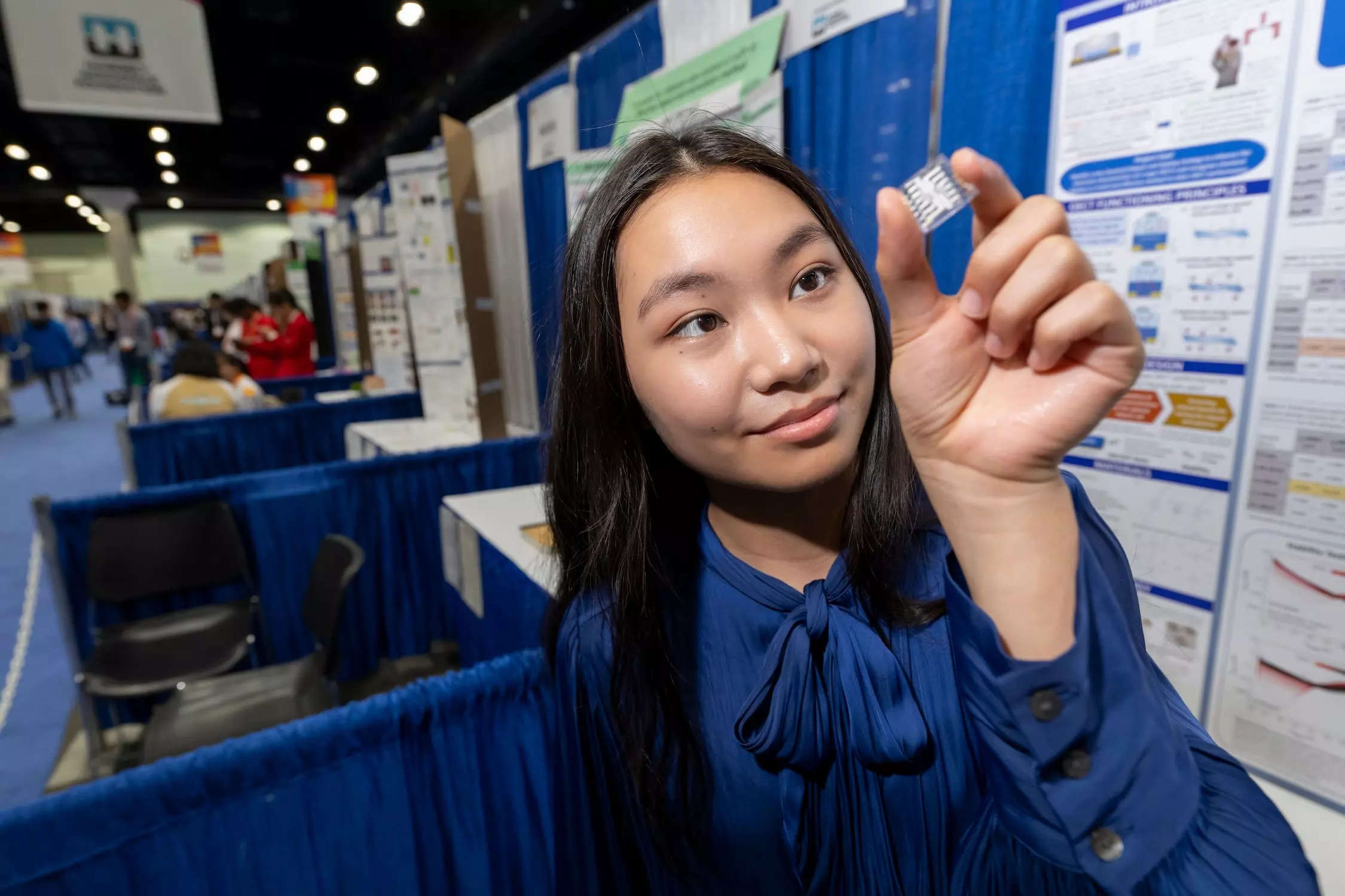 A girl in blue shirt with long dark hair holds a small OETC device that looks like a small clear square with white inside