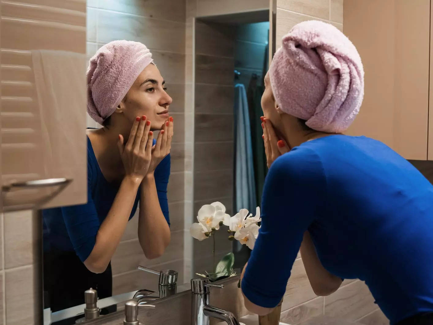 A woman wearing a towel on her head washing her face in front of the mirror