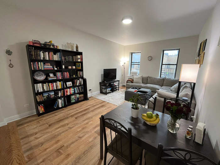 The living room features bookshelves, a TV, a sectional couch, an expandable dining table, and lots of empty space on the walls and floor.