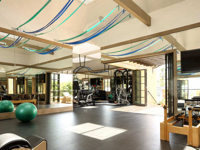 A gym with a weight training room, pilates reformer, band stretching area, massage room, and outdoor yoga terrace inside a Brentwood residence.