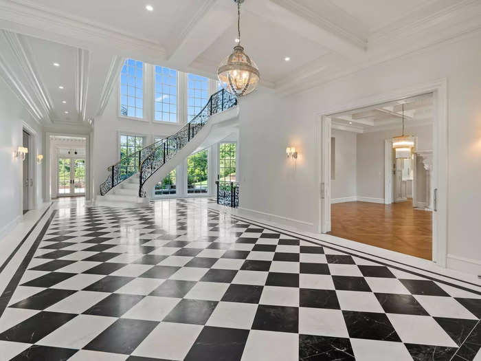 The foyer features black-and-white marble tiling, a chandelier, and 30-foot ceilings.