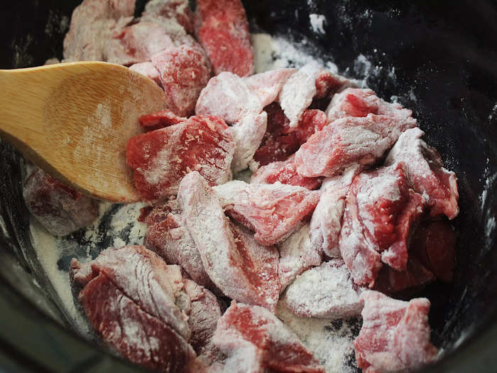 The first step is to toss your beef into the slow cooker and add the flour.