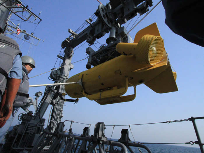 Unleashed from its restraints, the sailors guide the unmanned submersible over the side