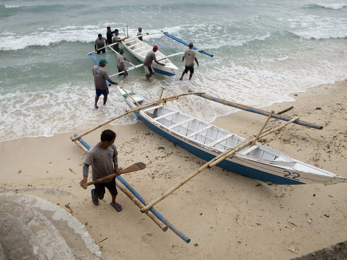 After a long day, fishermen pull their boats onto the beach.