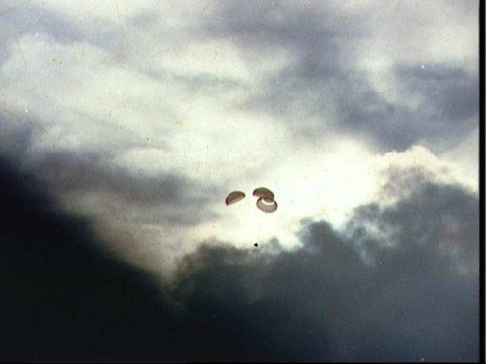 The capsule and its parachutes are visible after breaking through dark clouds.