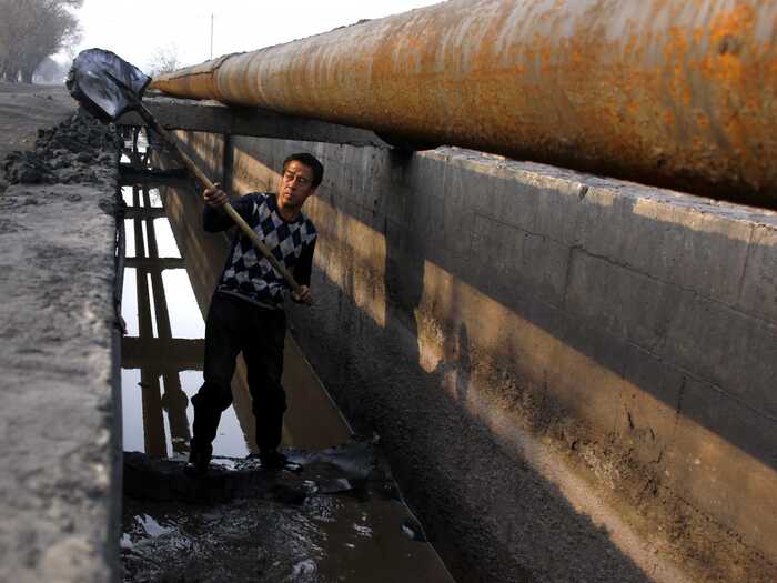 A miner shovels cast-off tailings (out of a channel sluicing crushed mineral ore containing rare earths) to a disposal dam on the edge of the Baotou.