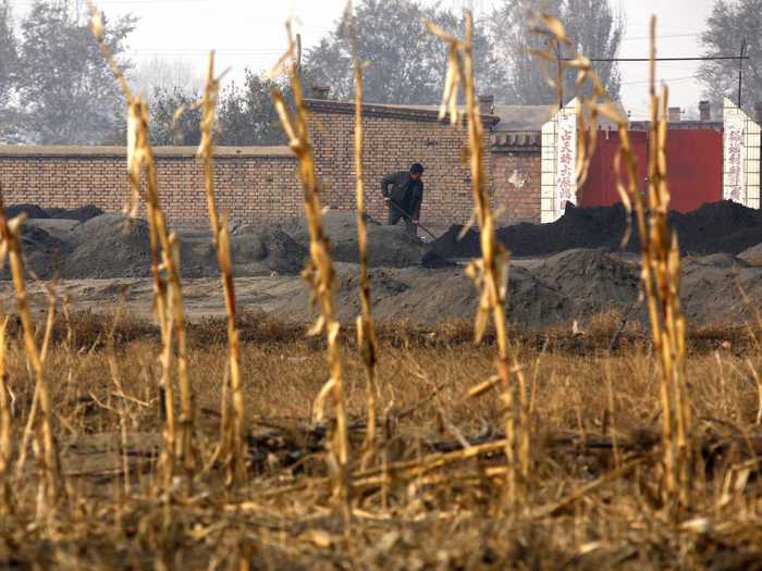 A villager is seen shoveling cast-off tailings of crushed ore that contain rare earths beyond a field of dead crops.