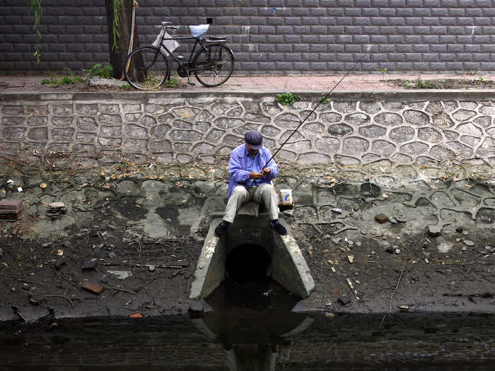 A fisherman sits on top of a drain at a polluted canal in central Beijing.