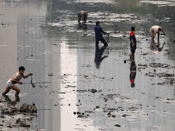 Fishermen walk through the muddy bottom of a polluted canal collecting fish in central Beijing.