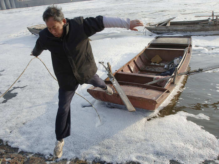 A fisherman jumps from his boat to the bank after fishing in the morning at a polluted river in Hefei, in east China