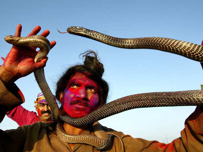 A snake charmer smeared with colored powder dances on a boat.