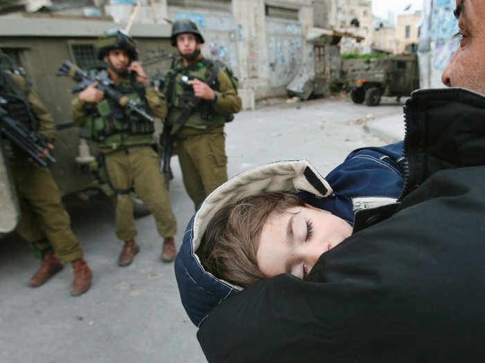 A Palestinian man carries a baby as he walks beside Israeli soldiers during an army raid in the West Bank city of Nablus February 26, 2007.