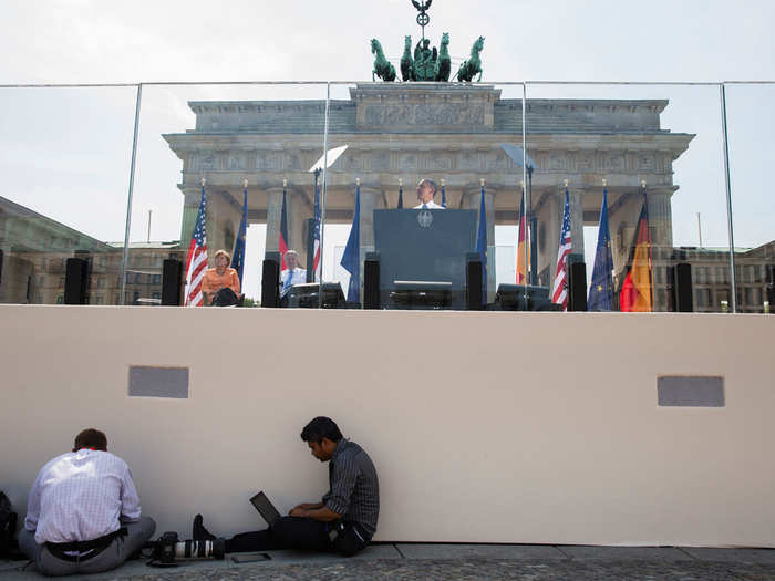 Photojournalists Evan Vucci and Jewel Samad work in the foreground as President Barack Obama delivers remarks at the Brandenburg Gate in Berlin.