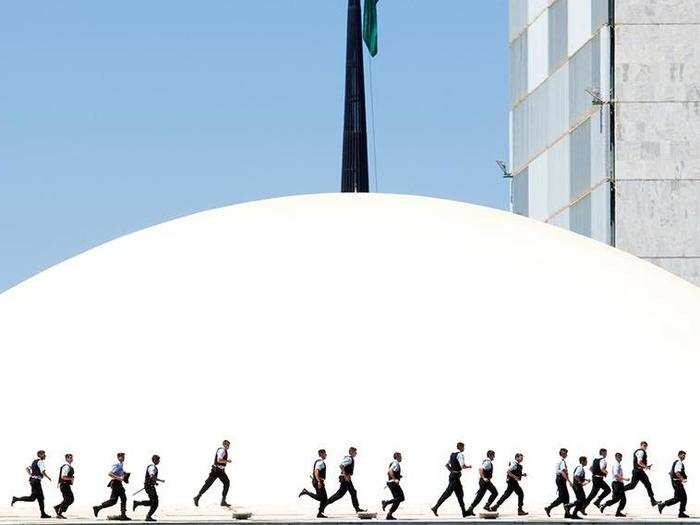 Police officers rush past the Brazilian National Congress to keep protestors against corruption from invading the building with brooms.