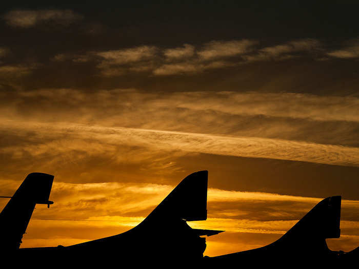 Tails of decommissioned aircraft sit against the backdrop of a setting sun.