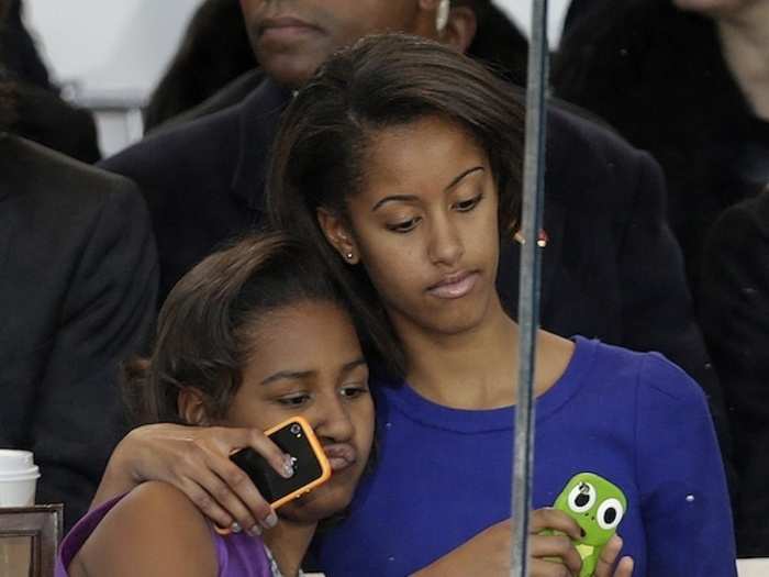 Sasha and Malia Obama snap photos of the parade with their iPhones.