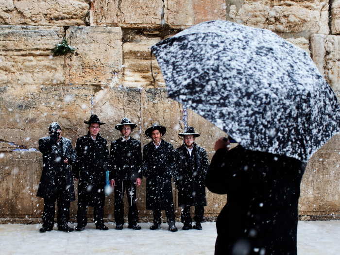 Snow falls as a group of Orthodox Jews pose for a snapshot next to the Western Wall