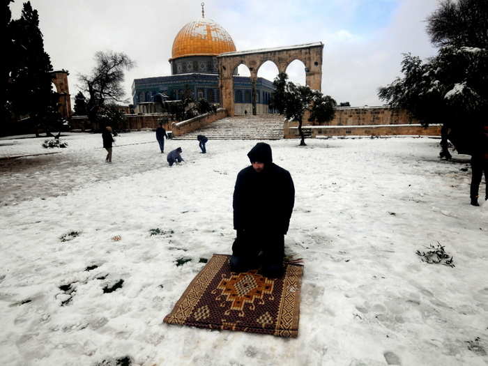 A Muslim man prays in the snow in front of the Dome of the Rock