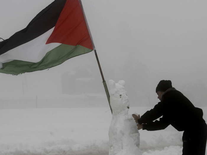 A Palestinian security officer adds finishing touches on a snowman decorated with a Palestinian flag in the West Bank city of Hebron