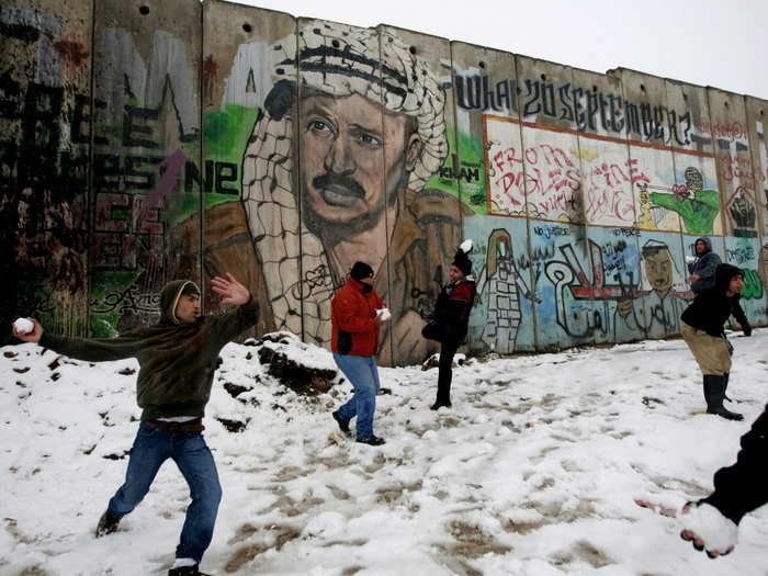 Palestinians play in the snow next to a section of Israel