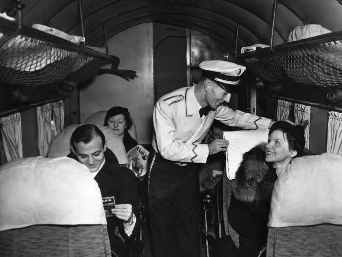 December 19, 1936 -  One of the first male stewards on a domestic airline makes a passenger comfortable at Newark Airport.