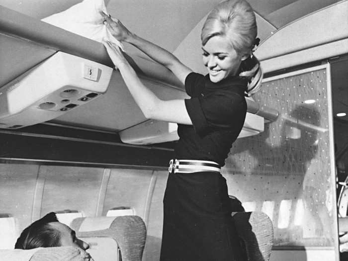 1967 - An American Airlines stewardess models her new uniform, a blue knit washable stretch dress with matching belt and hair bow. The skirt was allowed to be a scandalous 2-to-3 inches above the knee.