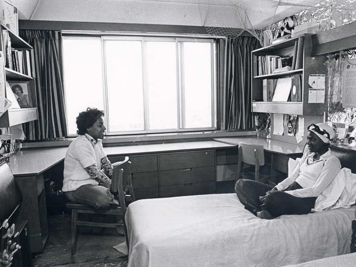 Two women catch up in a dorm room in this 1970s photo.
