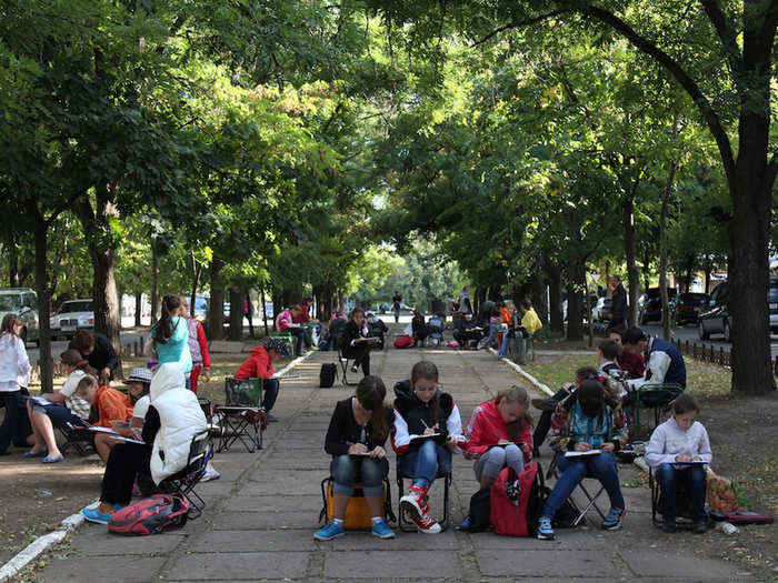 Children sketch in the park during an outdoors art class.