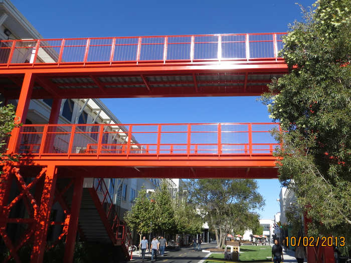 This pedestrian crosswalk, painted Golden Gate orange, was built as a fantasy. In Palo Alto, when Facebook grew to two buildings, employees had to cross a busy street. They wished for a crosswalk, so on their own campus, they built one.