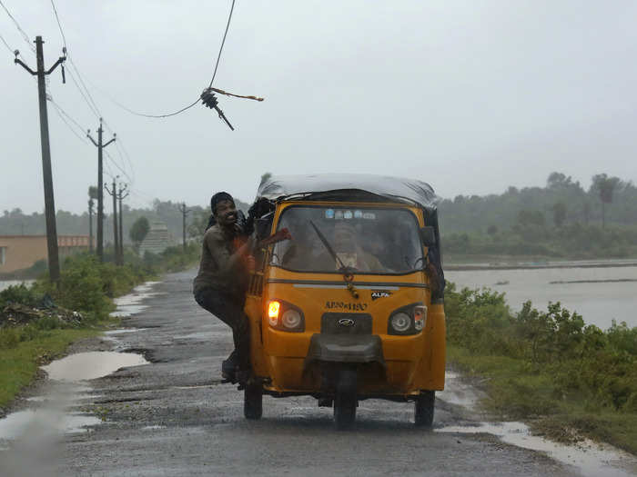 A man tries to avoid a broken electricity cable as he rides on an auto rickshaw to a safer place.