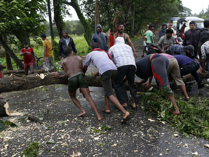 Men try to remove fallen trees from a road due to the rain and wind in the eastern Indian state of Odisha.