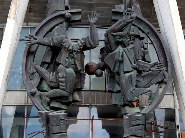 Above the entrance to the circus a crest is formed from the figures of two clowns, one of them now missing its head.