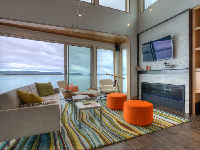 The wide fireplace is set in a wave-inspired plaster panel. The large aluminum framed windows offer sweeping views of the coast.