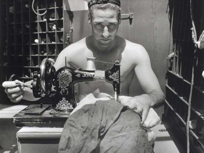 A Royal Navy sailor on board HMS Alcantara uses a portable sewing machine to repair a signal flag during a voyage to Sierra Leone in 1942.