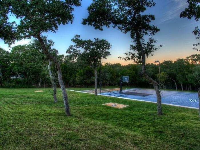 The court is surrounded by woods with several trees and a full grass yard.