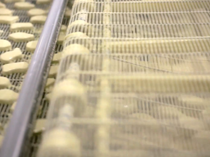 The chicken nuggets come out on the other side looking a bit like sugar cookies before they are sent into a fryer.