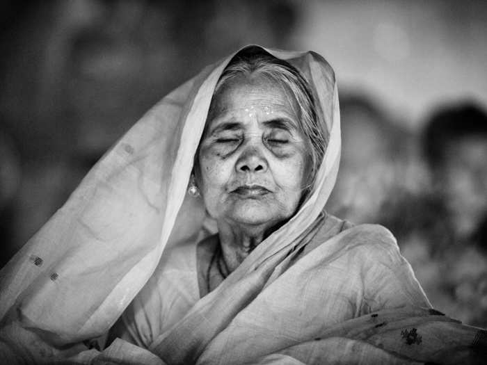 An old Hindu woman sits with lights and prays to God in front of the Shri Shri Lokanath Brahmachar Ashram temple.