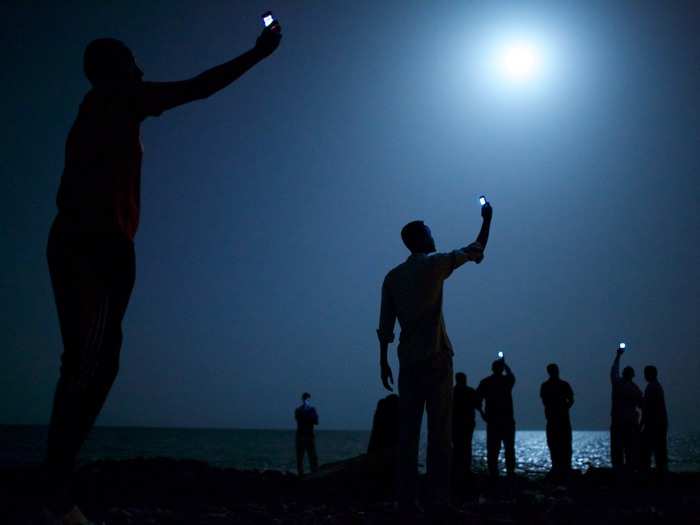 Djibouti City is a common stop for African migrants traveling  to Europe and the Middle East. Here, migrants on the shore raise their phones in an attempt to capture an inexpensive cellphone signal from Somalia to call back home.