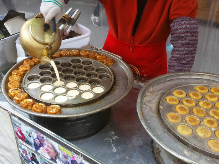 This woman poured batter from a tea kettle into a hot mold to make her tiny custard cakes.