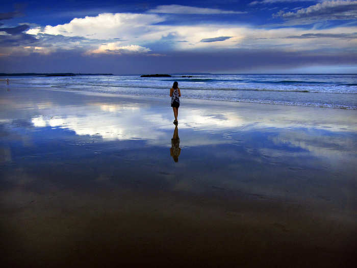 Storm clouds and dust can be seen in the sky above a woman as she walks at dusk along Mollymook Beach, south of Sydney.
