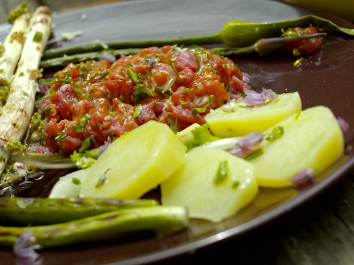 It includes fresh veal tartare, wild onions, horseradish, chives, salted leeks, cheese, and a flowered vinaigrette over the asparagus.