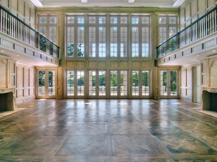 The room is huge. It has the 30-foot-high French limestone-paved walls with matching fireplaces on opposite sides. The wall of windows overlooks the pond, with the French doors opening to the waterside terrace.