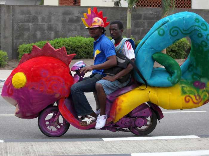 Two men ride a motorcycle disguised as a stuffed lizard motorcycle at a carnival in Nigeria.