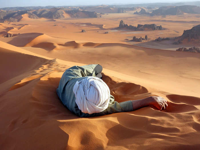 MERIT PRIZE: This photo was taken at the summit of Tin-Merzouga, the largest dune in the Tadrat region of the Sahara Desert in Algeria.  The man resting is  Moussa Macher, a Tuareg guide, who led the photographer and a group up the dune. The Tadrat region is famous for its red sand and rock paintings of animals that used to live there.