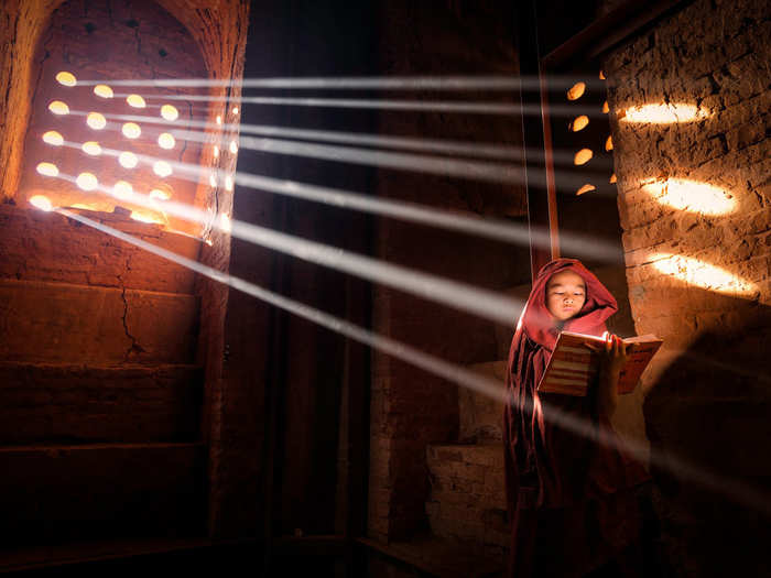 MERIT PRIZE: A young monk finds the perfect light source to read his book inside his pagoda in Old Bagan, Burma.