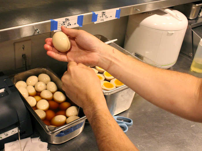 On the opposite side of the kitchen, a line cook halves hard-boiled eggs — another popular ramen topping — with a piece of fishing line attached to the counter.